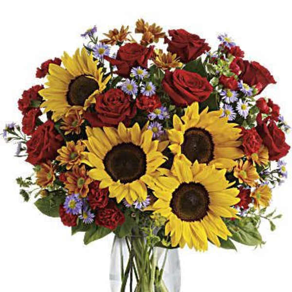 Bouquet of sunflowers, red roses, and small purple flowers in a clear glass vase