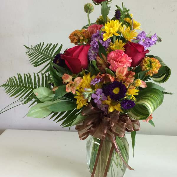 Mixed bouquet of roses, daisies, and purple flowers in a glass vase