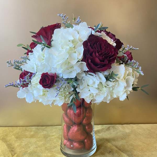 White hydrangeas and burgundy roses in a glass vase filled with red hearts