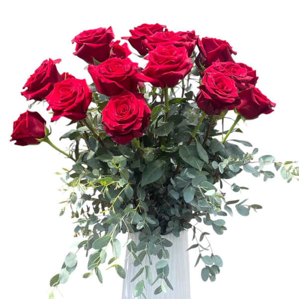 Red roses arranged in a white vase with trailing greenery