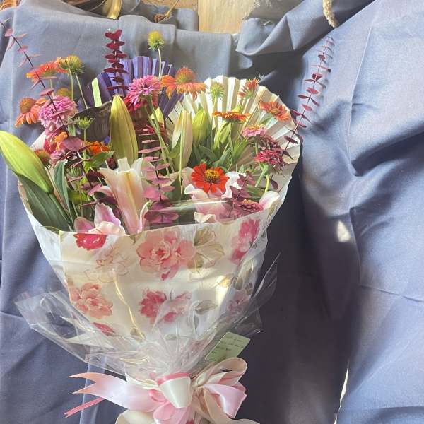 Bouquet of mixed flowers wrapped in floral paper with a pink ribbon