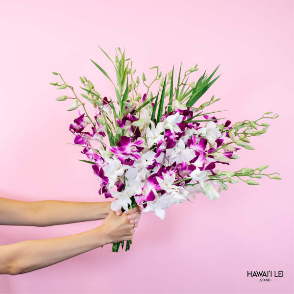 Handheld bouquet of white and purple orchids against a pink background