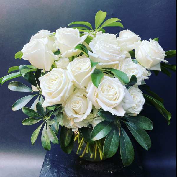 White roses arranged in a glass vase with green foliage
