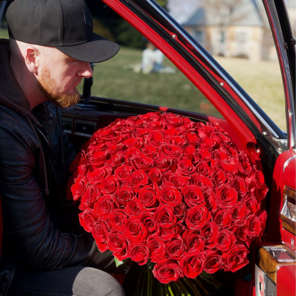 Large bouquet of red roses being held inside a red car
