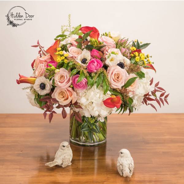 Mixed bouquet of roses, calla lilies, and white blooms in a glass vase