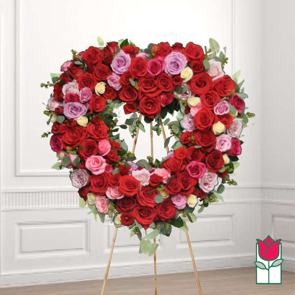Heart-shaped wreath of red, pink, and lavender roses on a stand