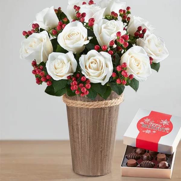 White roses in a tall vase with a box of chocolates beside it