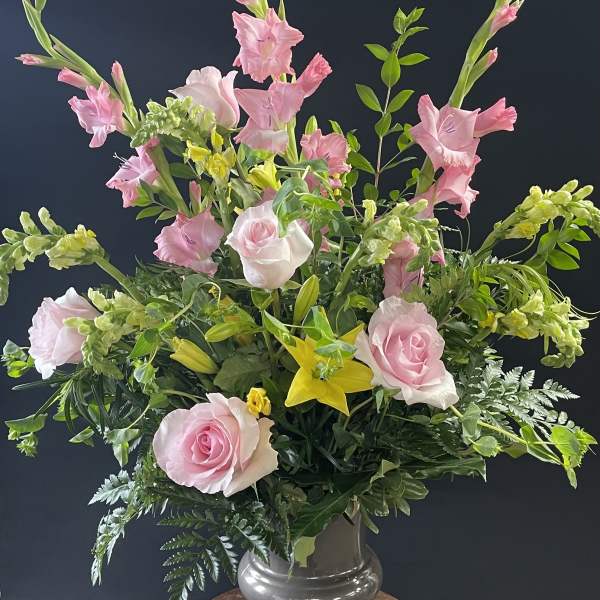 Pink roses and gladiolus in a glass vase with yellow lilies