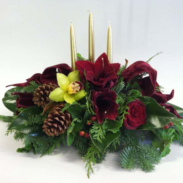 Low floral centerpiece with red blooms, pinecones, and gold candles