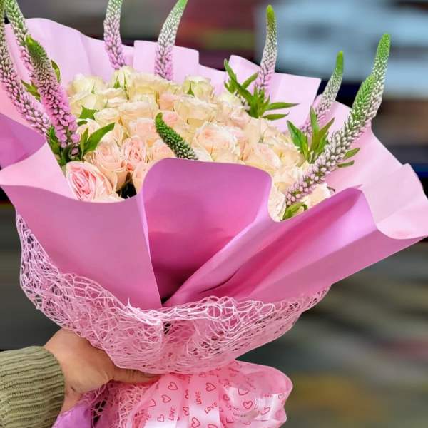 Pink bouquet of pale roses wrapped in pink paper with a heart ribbon