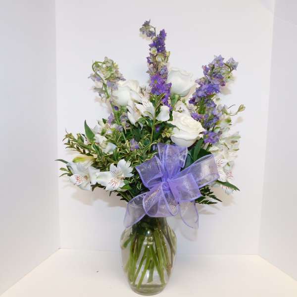 White and purple flower arrangement in a glass vase with a lavender bow