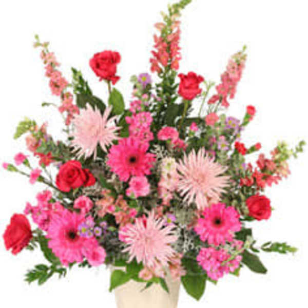 Pink and red mixed flower arrangement in a cream vase