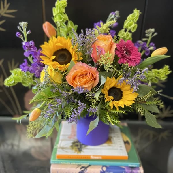 Colorful bouquet with sunflowers, orange roses, and purple flowers in a purple vase
