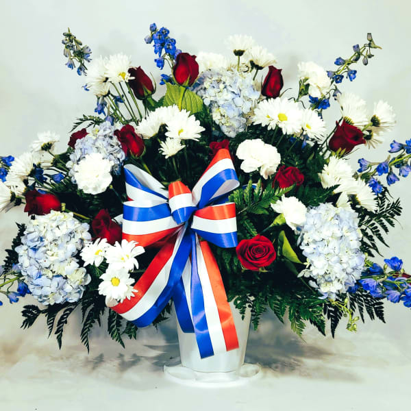 Large red, white, and blue floral arrangement in a white vase with a ribbon bow
