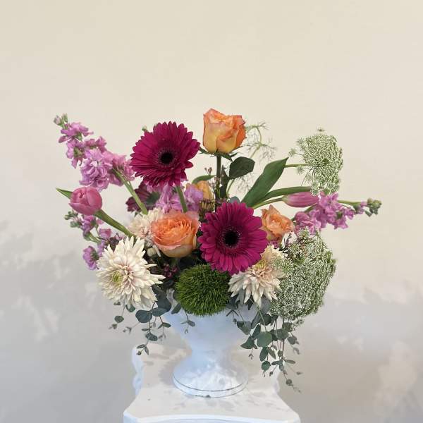 Mixed bouquet in a white pedestal vase with pink, orange, and white blooms