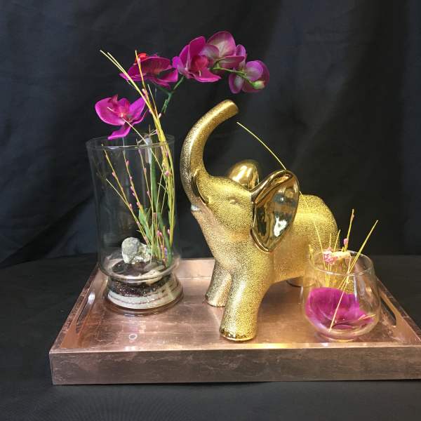 Gold elephant figurine with purple orchids in glass vases on a tray
