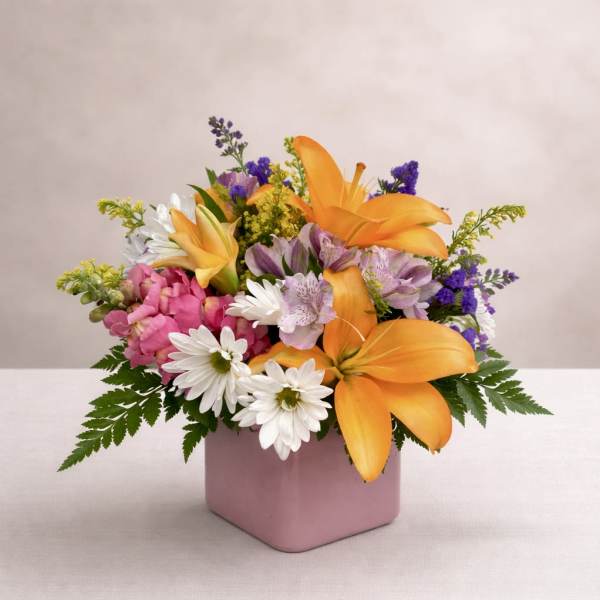Mixed bouquet of orange lilies, pink flowers, and white daisies in a pink vase