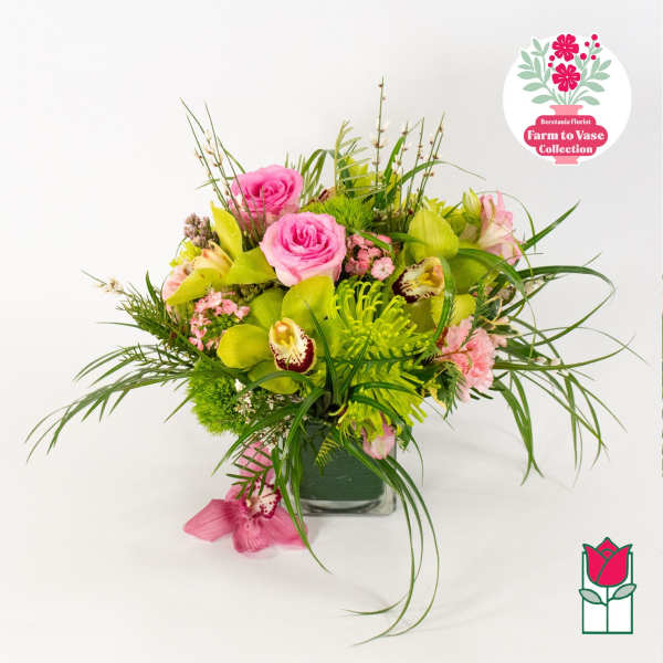 Pink roses and green orchids in a glass vase with long grass-like foliage