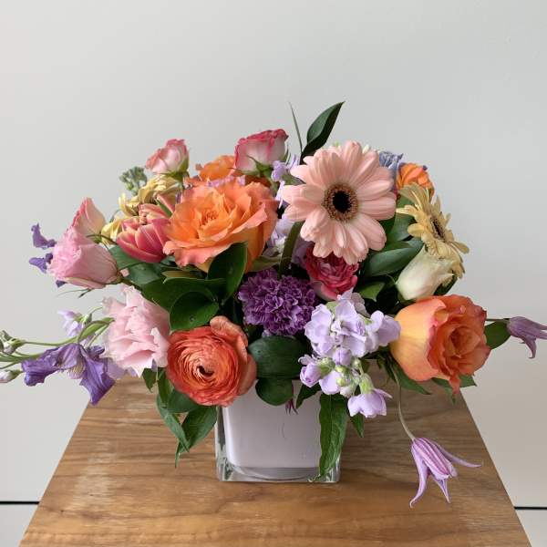 Mixed bouquet in a square glass vase with pink, orange, and purple flowers