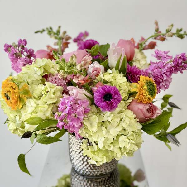 Mixed bouquet of pink, yellow, and green flowers in a textured vase