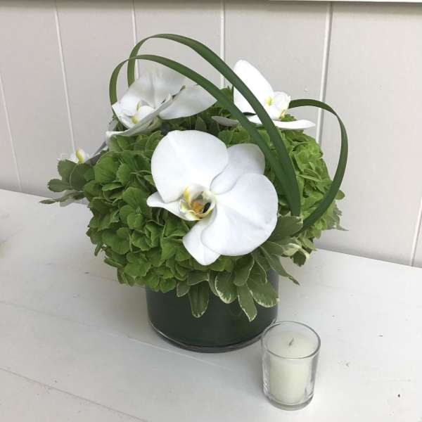 White orchids arranged in a green container with a small candle beside it
