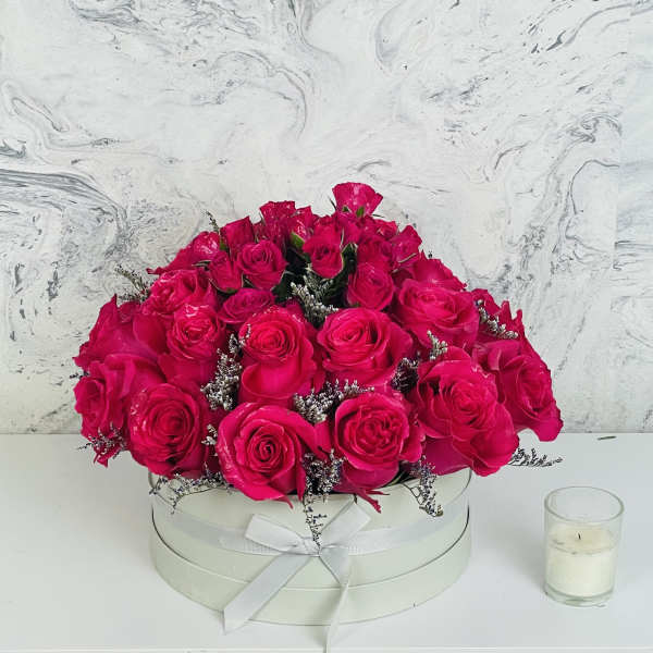Hot pink roses arranged in a round white box with a ribbon bow