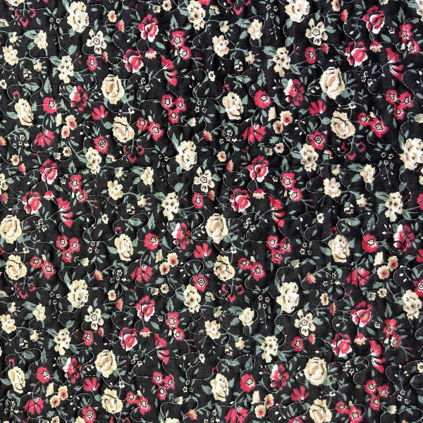 Black fabric with a dense floral print in pink, cream, and green