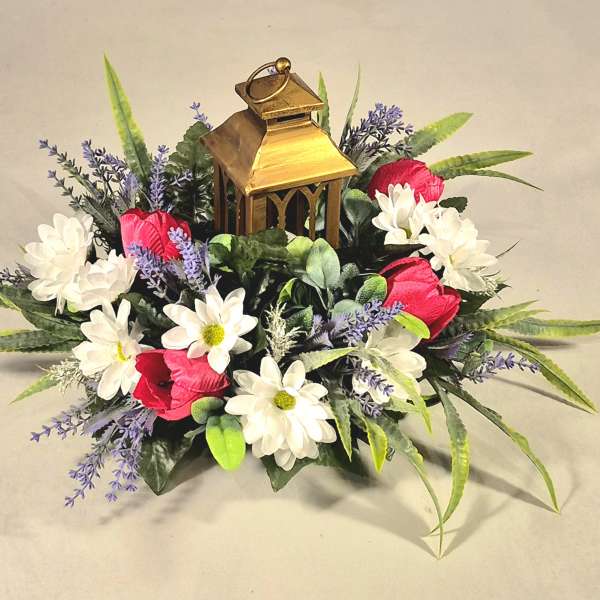 Floral arrangement with white daisies, red blooms, and a gold lantern centerpiece
