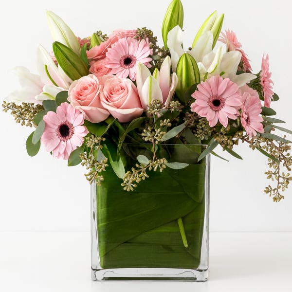 Pink roses and gerbera daisies in a clear square vase