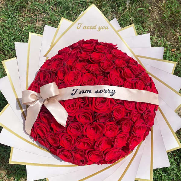 Round bouquet of red roses with a ribbon and apology message
