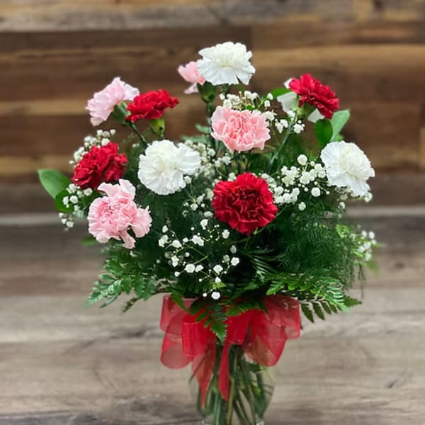 Bouquet of red, pink, and white carnations in a glass vase with a red ribbon
