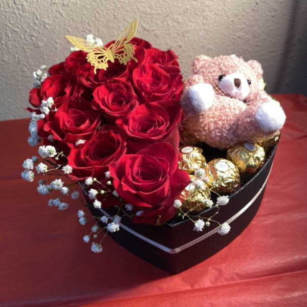 Heart-shaped box with red roses, a teddy bear, and chocolates