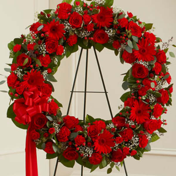 Red floral wreath on a black stand with a ribbon bow