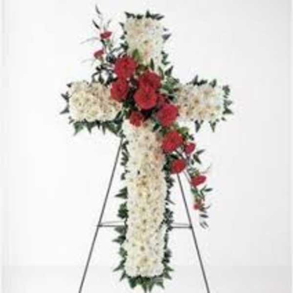 Cross-shaped floral funeral spray with white flowers and red roses on a stand