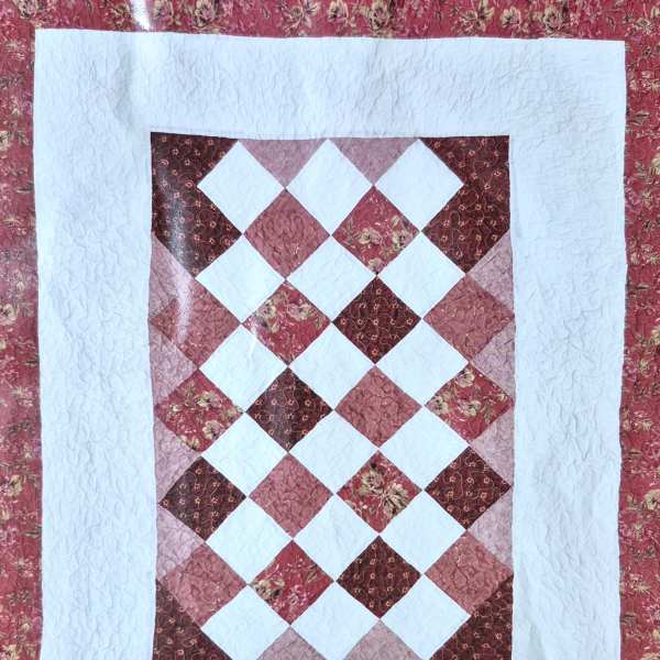 Patchwork quilt with a diamond pattern in pink, red, and white