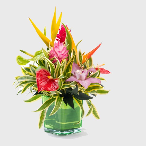 Tropical flower arrangement in a green glass vase with pink and yellow blooms