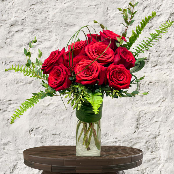 Red roses arranged in a clear glass vase with greenery
