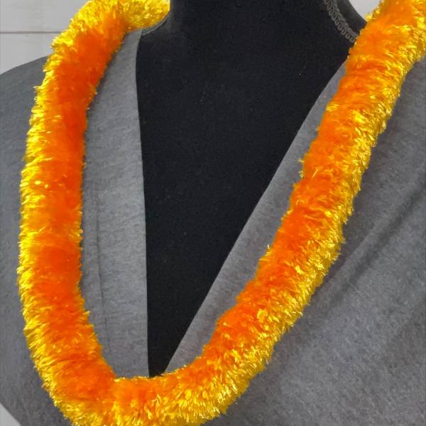 Orange and yellow fluffy lei necklace displayed on a gray-draped black mannequin.