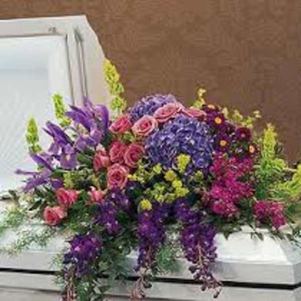 Colorful floral arrangement on a white casket with purple, pink, and blue blooms.