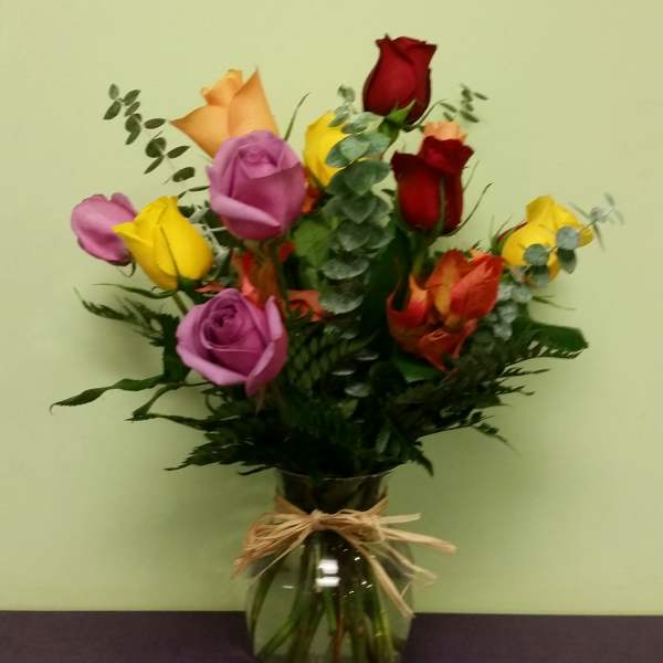 Bouquet of multicolored roses in a glass vase with a raffia bow