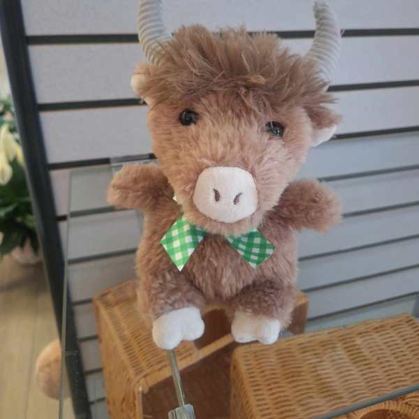 Small brown plush cow with curled horns and a green checkered bow displayed on a glass shelf.