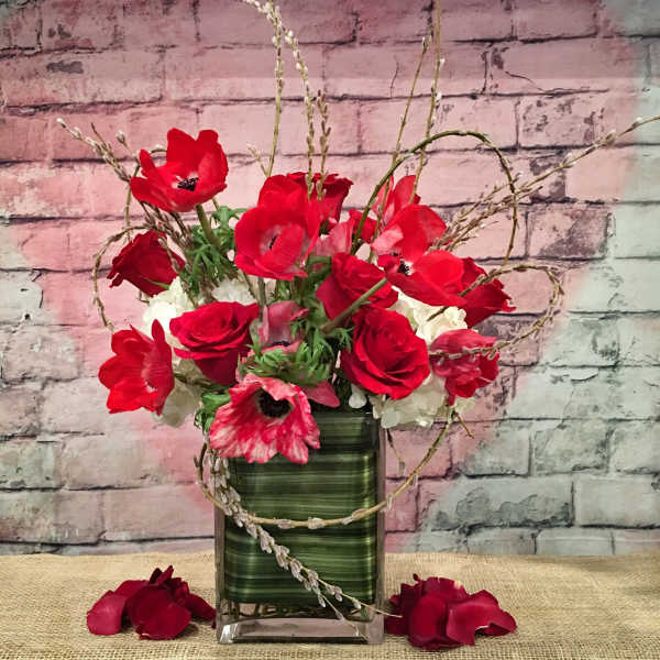 Red poppies and roses in a green glass vase with white blooms