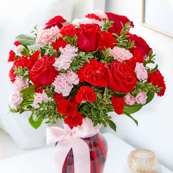 Red roses and pink carnations in a red glass vase with a pink ribbon