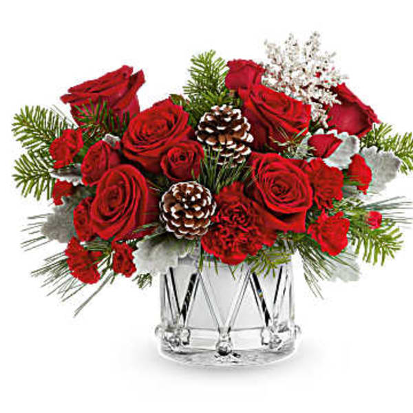 Red roses arranged in a clear glass vase with pinecones and winter greenery