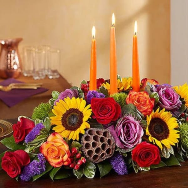 Low floral centerpiece with lit orange candles and sunflowers
