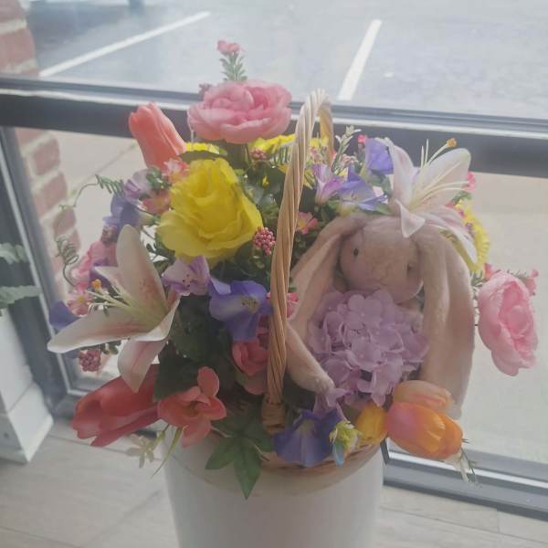 Basket of mixed pink, yellow, and purple flowers with a plush bunny tucked among the blooms