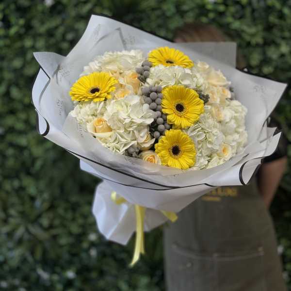 Bouquet of yellow gerbera daisies and white roses wrapped in white paper