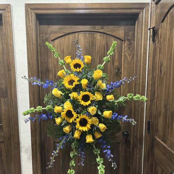 Standing floral spray with yellow sunflowers and roses accented by blue flowers
