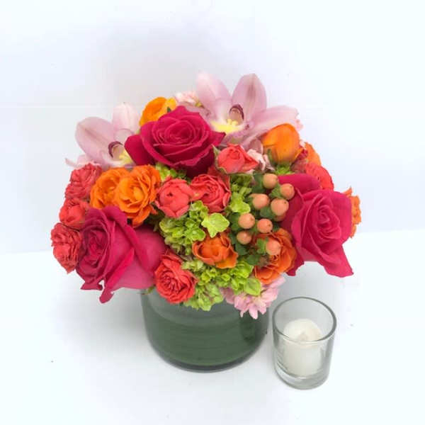 Bright mixed bouquet in a green vase with a small candle beside it