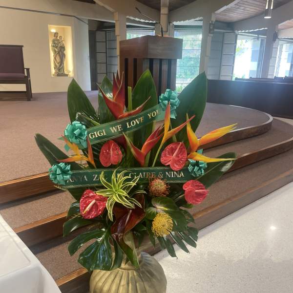Tropical floral arrangement with red and orange blooms in a gold vase